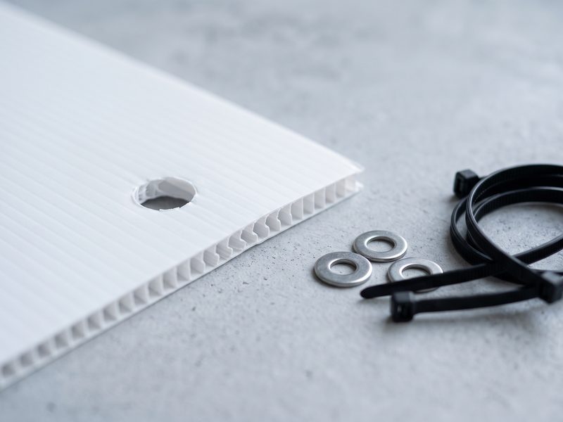 A Correx panel with a drilled corner fixing hole, beside stainless washers and cable ties.